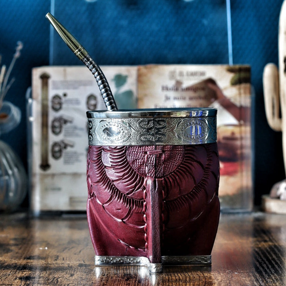 Face artisanale du maté Imperial : cuir bordeaux ciselé, bande centrale abstraite et virole lisse en maillechort brillant sur base à quatre pieds.