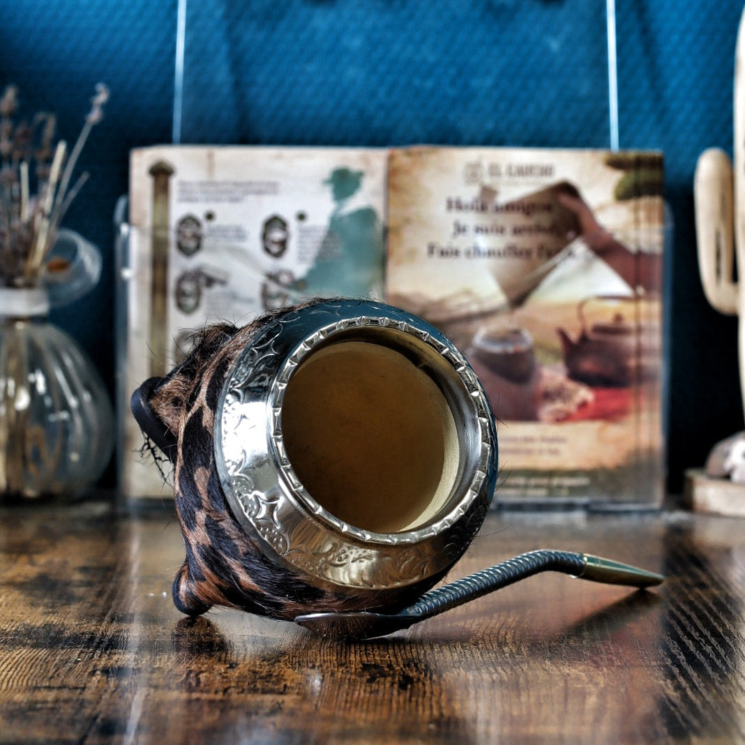 Maté de forme Torpedo artisanal en calebasse naturelle avec un double revêtement en cuir et motif Animal Print, surmonté d'une virole finement ciselée, présenté avec sa bombilla.