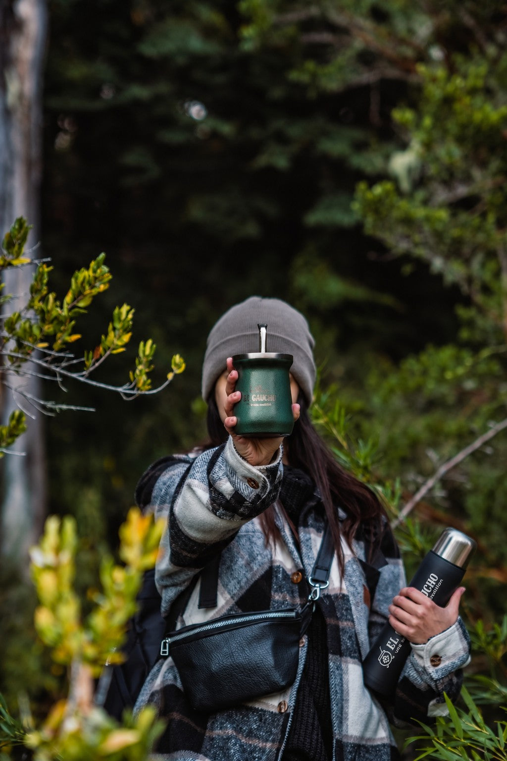 En forêt, le Mate Listo El Gaucho en mode thermos avec sa tasse en inox, à côté d'un maté El Gaucho vert